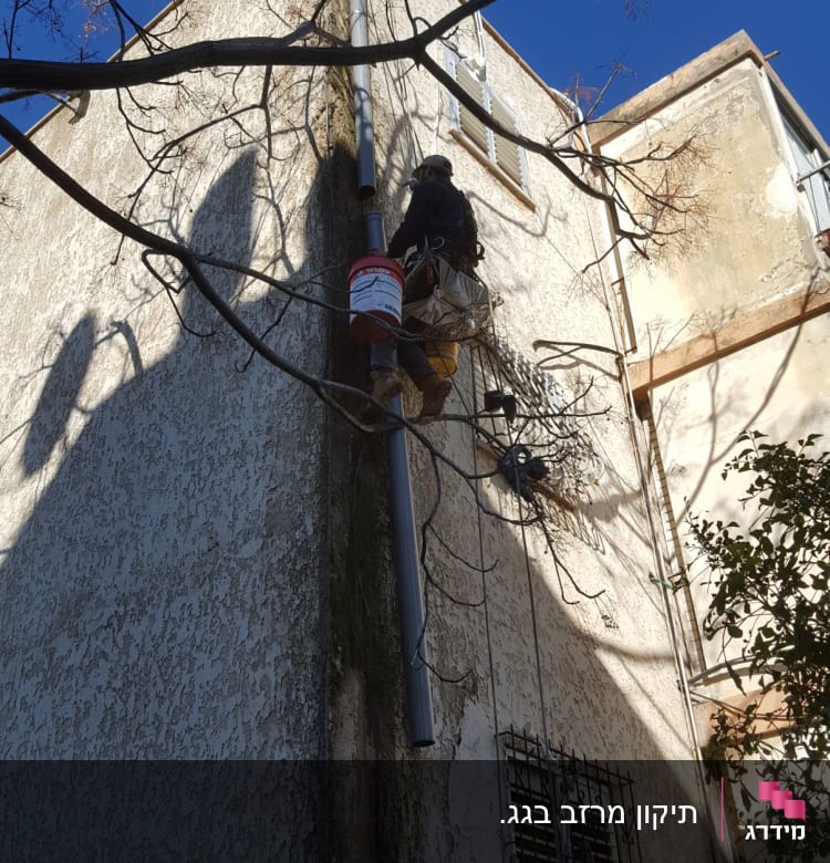 אדם מטפס על קיר עם דלי ליד גג